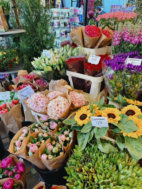 An assortment of fresh flowers and floral arrangements displayed at a local flower shop, including vibrant sunflowers with large yellow petals and dark centers, bouquets of cream-colored lilies with l